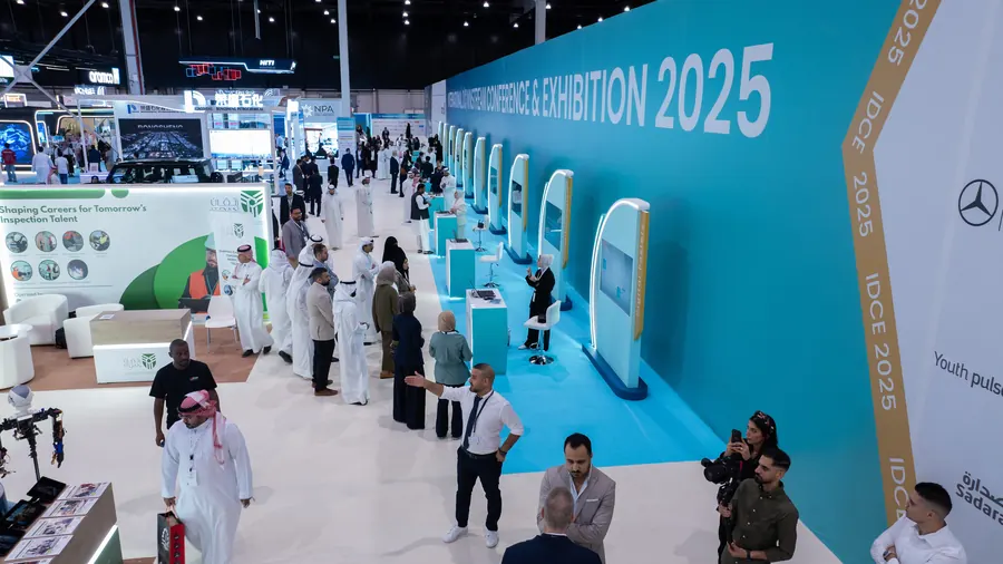 Visitors walking the exhibition hall past the event's branded wall
